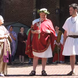 The cast of the play Julius Caesar, with Caesar at the center, performs a scene in the plaza of the Eugene Saturday Market.